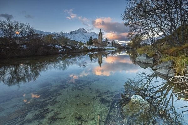 Dawn illuminates the snowy peaks and the bell tower reflected in Lake Sils, Engadine