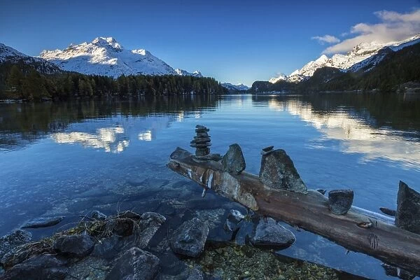 Dawn illuminates the snowy peaks reflected in the calm waters of Lake Sils, Engadine