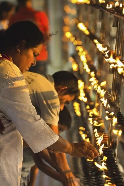 Devotee lighting candles at sunset in the Temple of the Sacred Tooth Relic
