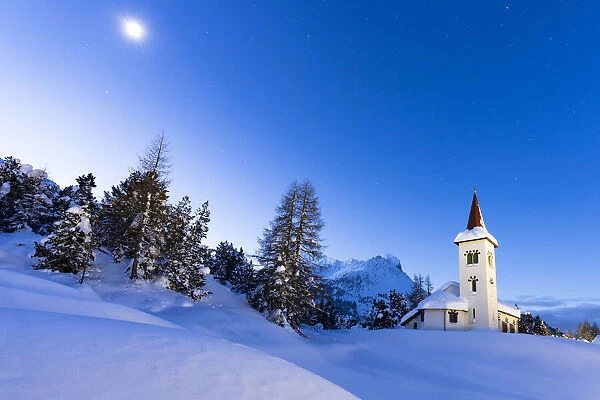 Dusk over Chiesa Bianca in the snowy landscape lit by moon, Maloja, Bregaglia Valley