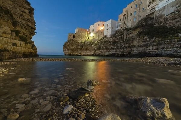 Dusk lights on the clear sea framed by the old town perched on the rocks, Polignano a Mare