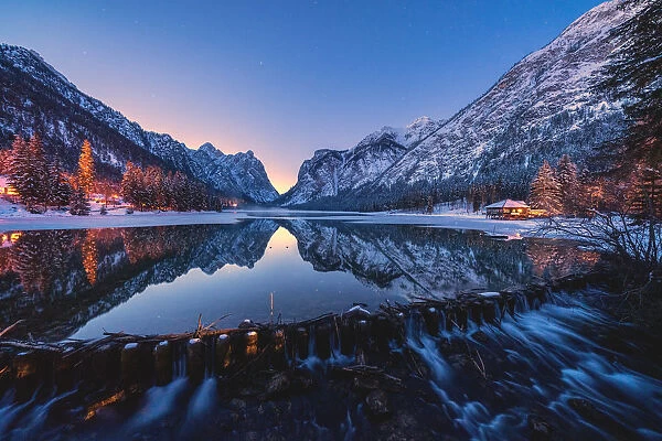 Dusk lights on the snowy peaks mirrored in Lake Dobbiaco, Val Pusteria, Dolomites