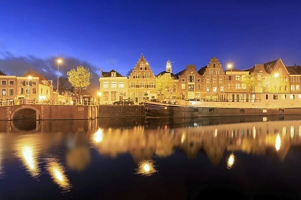Dusk lights on typical houses and bridge reflected in a canal of the River Spaarne