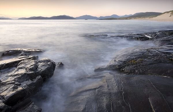 Dusk view across open water towards Taransay and North Harris from the rocky shore at Borve