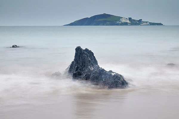 A dusk view of shoreline rocks on the beach at Bantham, with a view towards Burgh Island and its hotel, on the south coast of Devon, England, United Kingdom, Europe