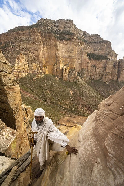Ethiopian priest leaning on steep rocks leading to Abuna Yemata Guh church