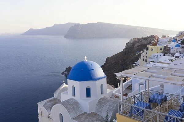 Evening view over the Caldera from Oia with blue domed church and distant volcanic cliffs