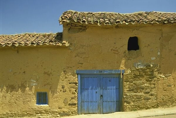 Exterior of an adobe house with a tile roof and blue door