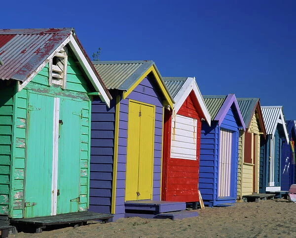 Exterior of a row of beach huts painted in bright primary colours, Brighton Beach
