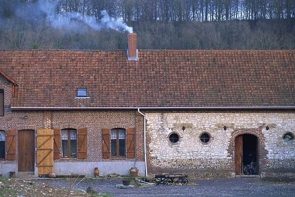 Exterior of a single storey house in the countryside, with smoking chimney