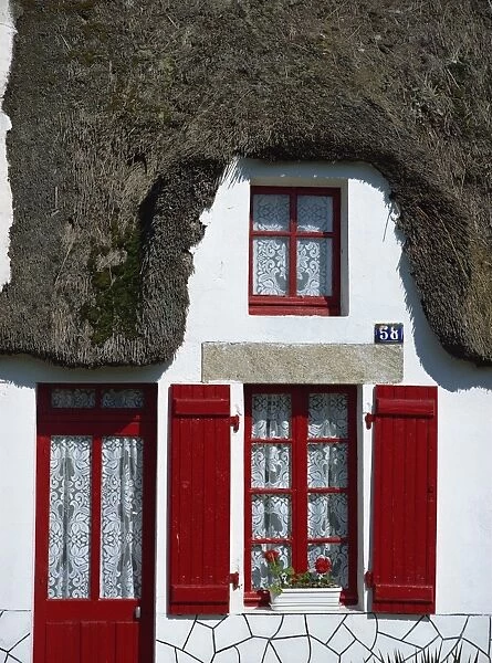 Exterior of a thatched cottage with red door and shutters in La Grande Briere