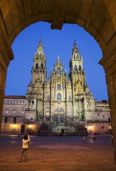 Facade of cathedral seen from Praza do Obradoiro floodlit at night, with a woman taking a photograph, Santiago de Compostela, UNESCO World Heritage Site, Galicia