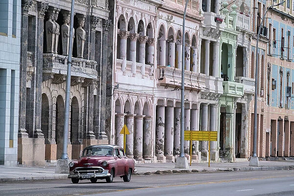 Faded grandeur, stucco, weather-beaten houses on seafront of Malecon, with red classic car, Havana, Cuba, West Indies, Caribbean, Central America