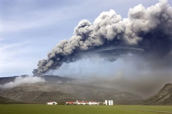 Farm buildings and green fields with the ash plume of the Eyjafjallajokull eruption in the distance