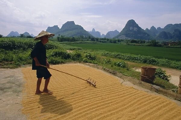Farmer turning grain, near Yangshuo, Guangxi Province, China