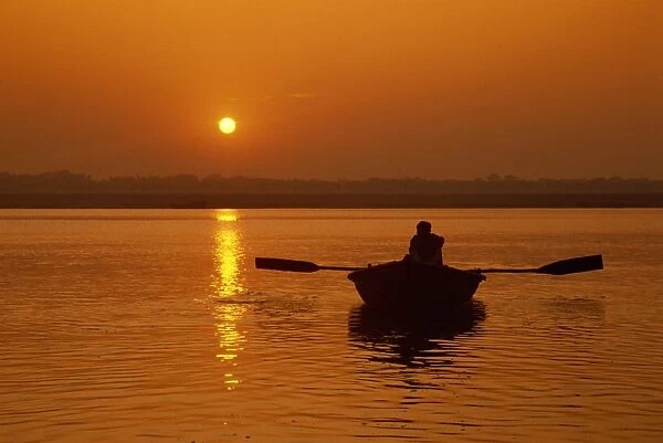Figure in rowing boat silhouetted at sunset