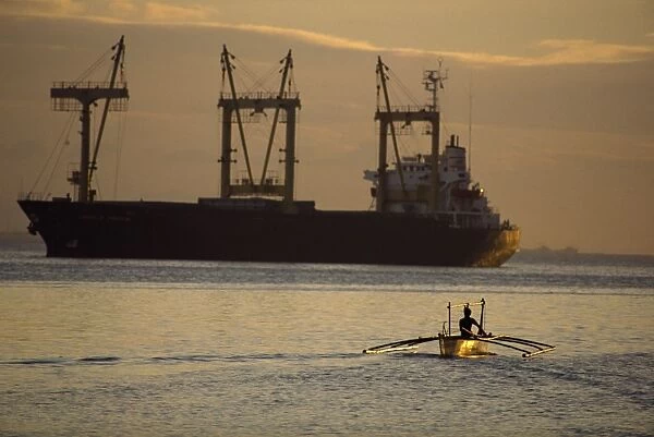 Figure silhouetted at dusk in an outrigger canoe near huge cargo ship