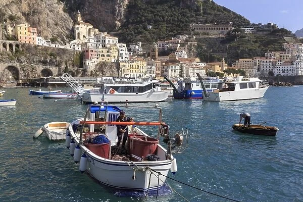 Fisherman in fishing boat in Amalfi harbour, from quayside with view towards Amalfi town