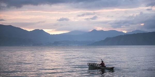 Fisherman in a fishing boat on Lake Toba (Danau Toba) at sunrise, North Sumatra, Indonesia