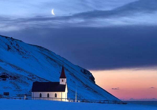 Floodlit church at dawn against snow covered mountains, winter, near Vik, South Iceland