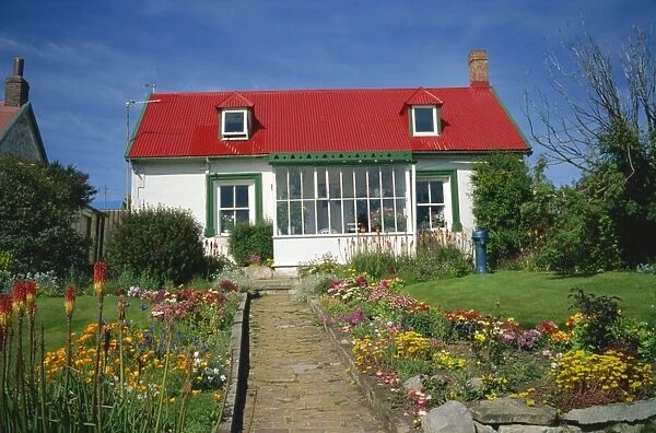Flower beds line a brick path up to a typical private house, with bright red corrugated roof