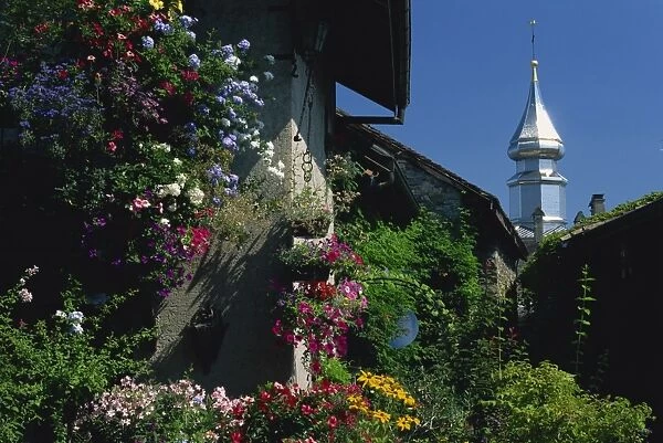 Flower filled garden of village house with sparkling church spire beyond