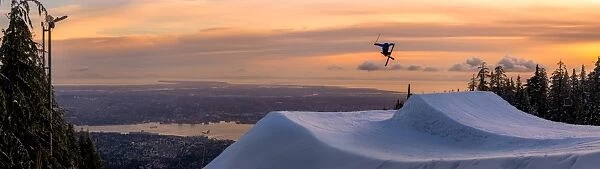 Freestyle skier doing a trick off a jump above city at sunset, Canada, North America