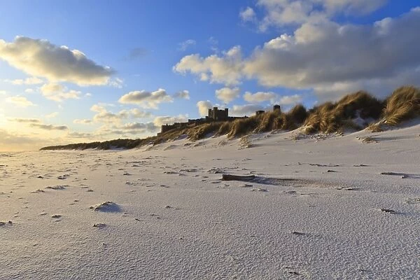 Fresh Spring snow at dawn highlight ripples and marks in the sand beneath Bamburgh Castle, Bamburgh, Northumberland, England