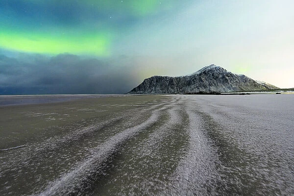 Frozen sand of Skagsanden beach under northern lights (aurora borealis) in winter