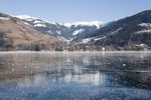 Frozen Zeller See lake with snow capped mountains reflected in ice in alpine resort