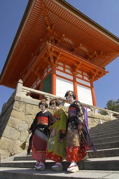 Three geishas in traditional dress walking down steps