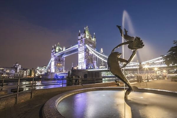 The Girl With A Dolphin Fountain frames Tower Bridge reflected in the River Thames at night