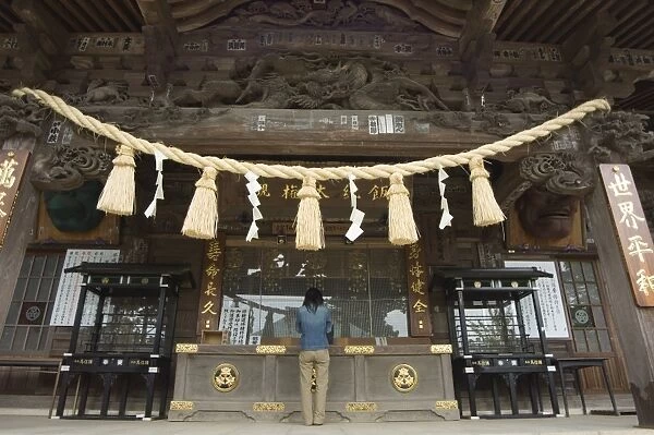 Girl praying at shrine under giant rope