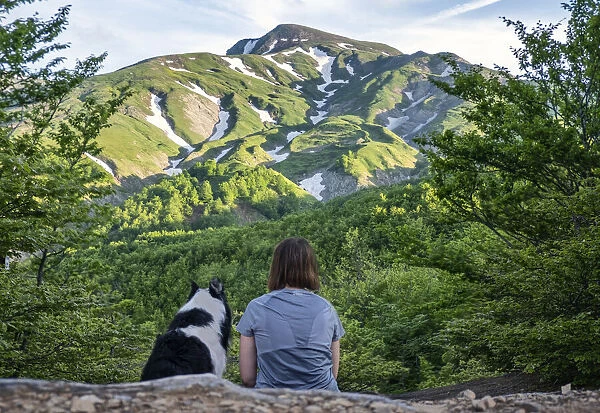A girl sitting beside her border collie dog staring at a mountain landscape of Cusna Mountain, Emilia Romagna, Italy, Europe