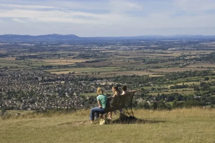 Framed Print : Three girls sitting on bench looking at the view over Bishops Cleeve village Framed Print : Three girls sitting on bench looking at the view over Bishops Cleeve village