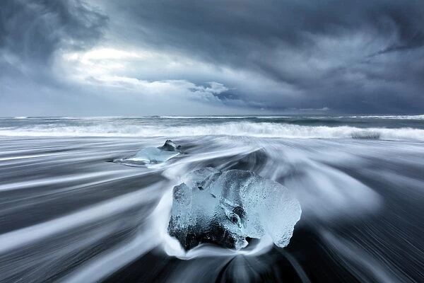 Glacier ice on black sand beach with waves washing up the beach on a stormy winter day