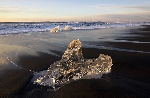 Glassy pieces of ice on volcanic black sand beach at sunrise, near Jokulsarlon Lagoon