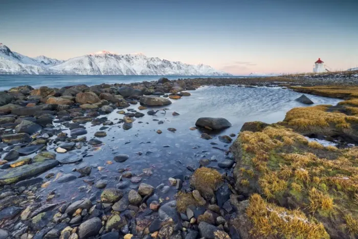 Framed Print : Grass and rocks frame the lighthouse surrounded by frozen sea and snowy peaks at dawn Framed Print : Grass and rocks frame the lighthouse surrounded by frozen sea and snowy peaks at dawn