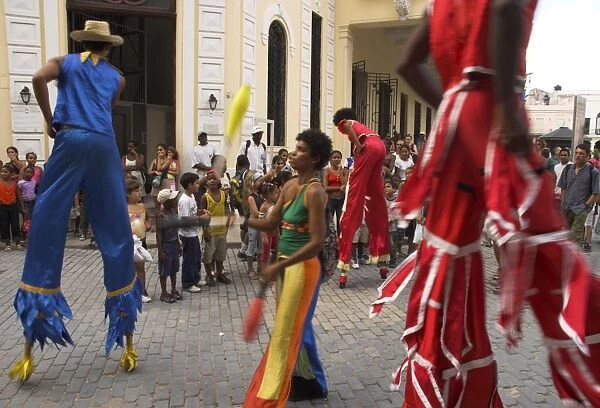 Group of people on stilts and in colourful costumes dancing and juggling in the street