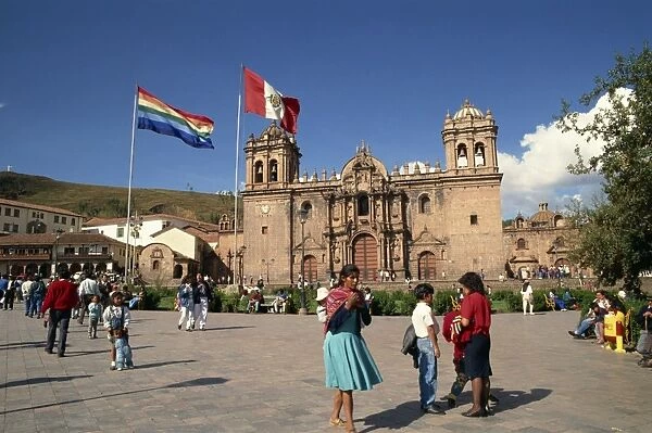 Groups of people and flags flying in front of the cathedral in Cuzco