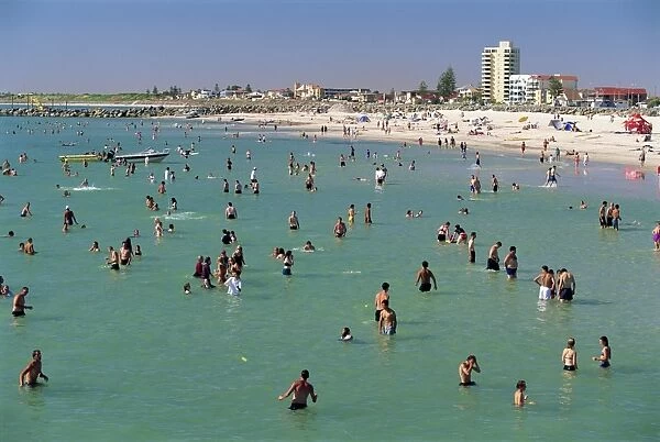 Groups of people in the sea and on the beach at Glenelg, a resort suburb of Adelaide