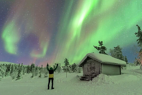 Happy tourist waving at the Northern Lights (Aurora Borealis) dancing in the night sky above the Arctic Circle, Akaslompolo, Kolari municipality, Finland, Europe