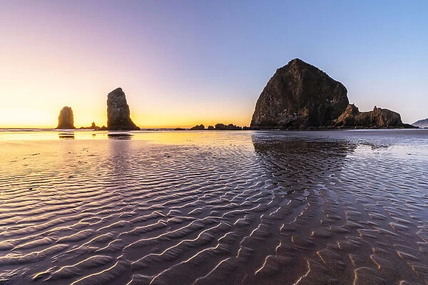Haystack Rock and The Needles at sunset, with textured sand in the foreground