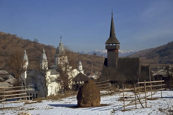 Haystack in snow covered field with two churches in the background at Botita village