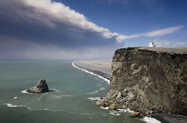 Headland with lighthouse at Dyrholaey looking towards a black volcanic sand beach stretching 15 miles into the distance and the ash plume of the Eyjafjallajokull eruption, near Vik i Myrdal, southern area, Iceland