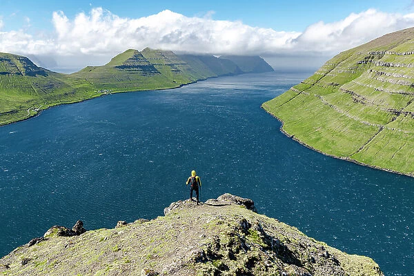 High angle view of hiker admiring mountains and ocean standing on top of a mountain, Klaksvik, Bordoy Island, Faroe Islands, Denmark, Europe