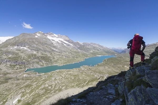 Hiker admires the blue alpine lake from Pizzo Campaccio, Bernina Pass, Canton of Graubunden