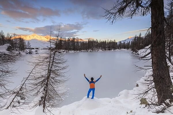 Hiker admires Lago Azzurro completely frozen at dawn, Spluga Valley, Province of Sondrio