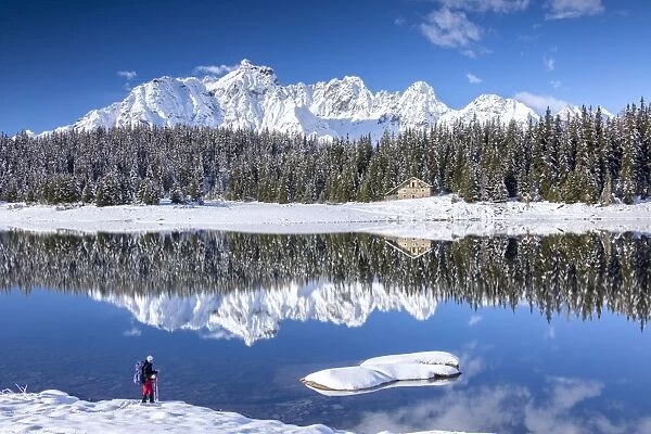 Hiker admires the snowy peaks and woods reflected in Lake Palu, Malenco Valley, Valtellina