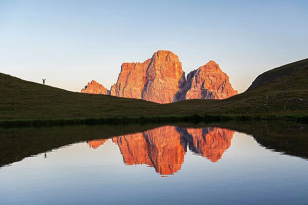 Hiker admires the sunset in front of the giant massif of Pelmo mountain reflected in the water of the small lake of Baste, Giau Pass, Cortina d'Ampezzo, Dolomites of Belluno, Veneto, Italy, Europe